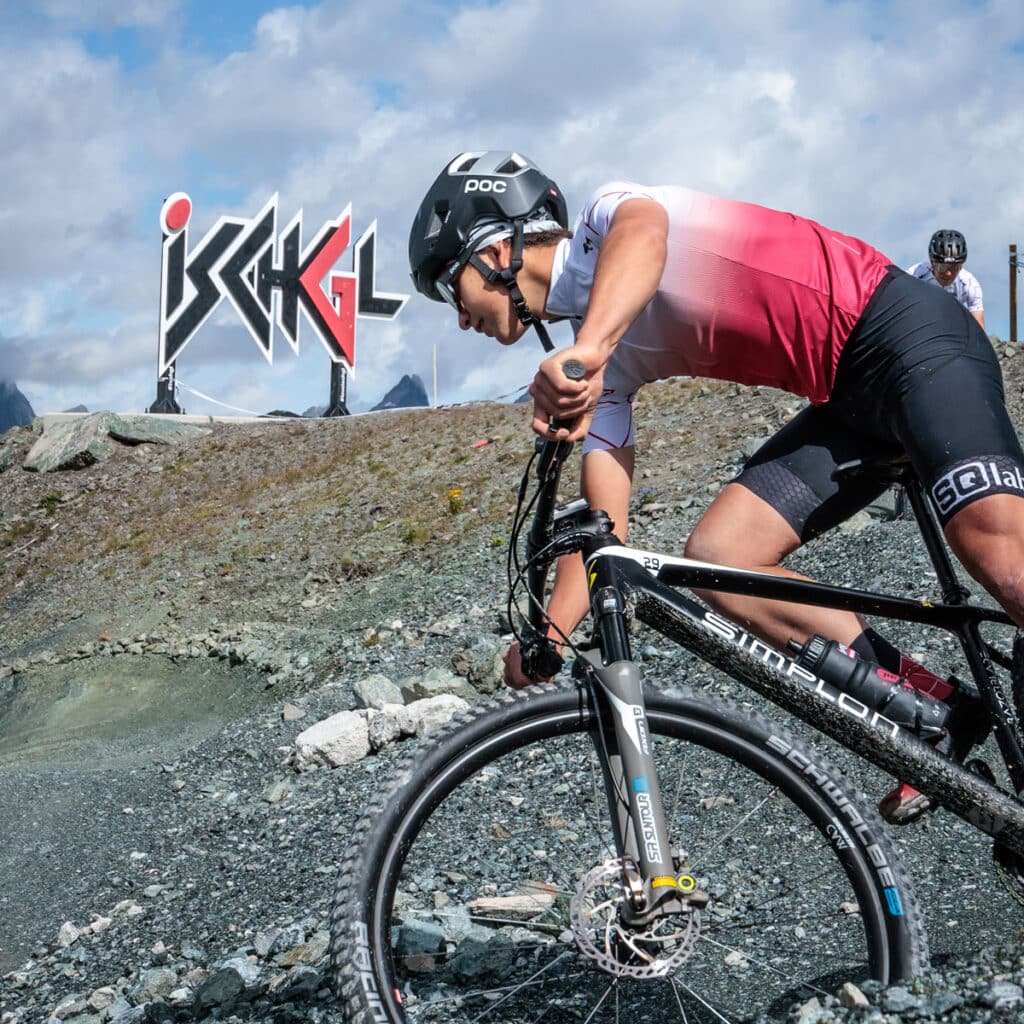 Radfahrer fährt auf felsigem Terrain in der Nähe eines großen Ischgl-Schildes - Sommerurlaub in Ischgl erwartet Sie.