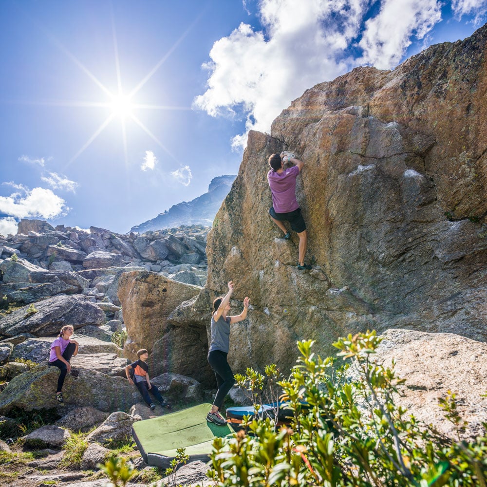 Vier Personen genießen das Bouldern an Felsen unter der strahlenden Sonne während ihres Sommerurlaubs in Ischgl.