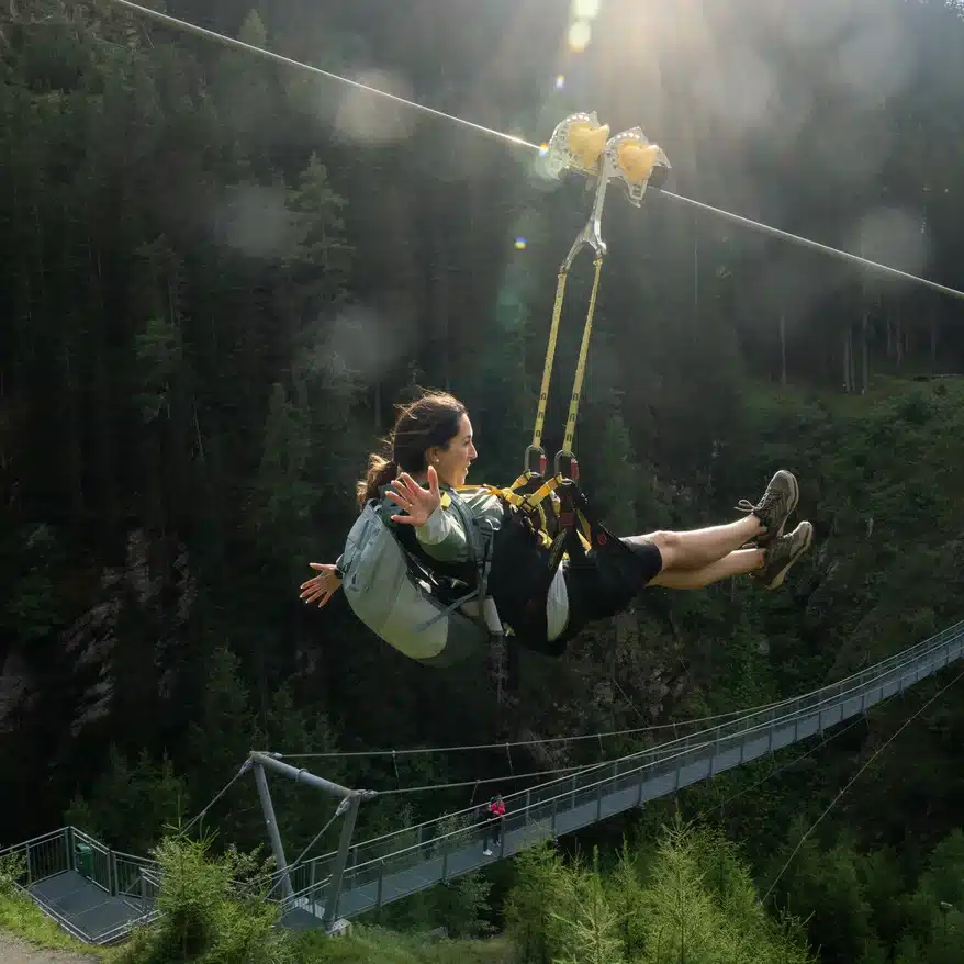 Abenteurer beim Ziplining über ein üppiges Tal und eine Hängebrücke im Sommerurlaub in Ischgl.