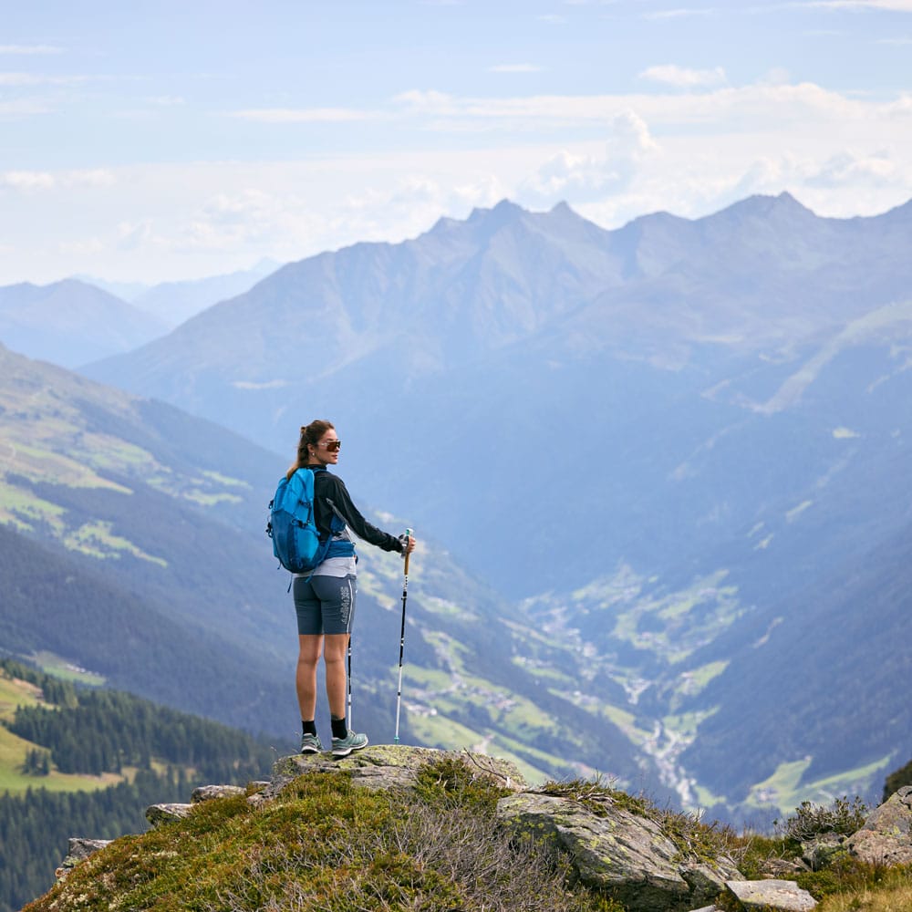 Wanderer mit Rucksack auf einem Berg stehend, Sommerurlaub im malerischen Tal von Ischgl genießend.
