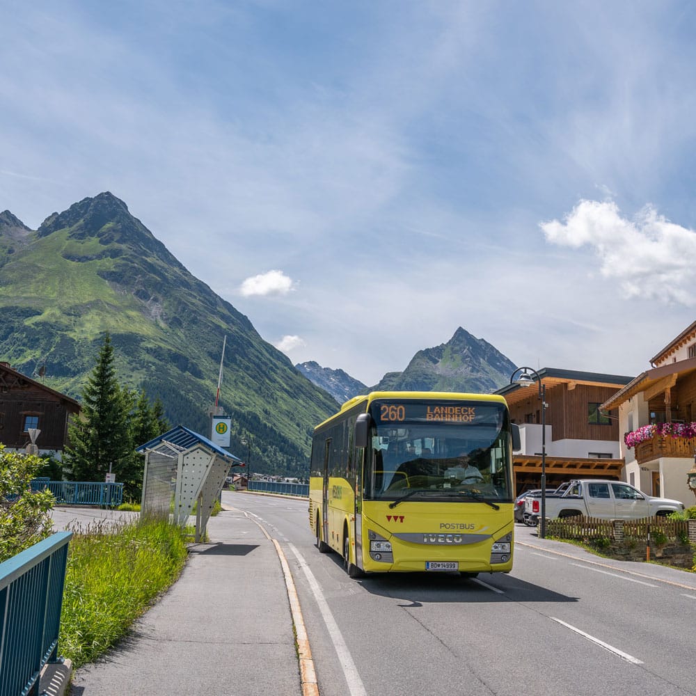 Ein gelber Bus fährt auf einer Straße in einem Bergdorf, perfekt für einen Sommerurlaub in Ischgl.