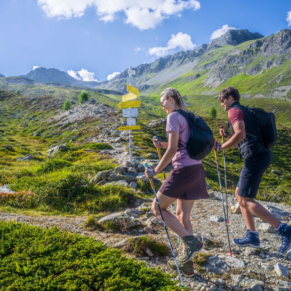 Zwei Wanderer gehen auf einem felsigen Pfad bergauf und genießen ihren Sommerurlaub in den grünen Bergen von Ischgl.